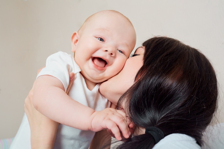 Beba se smeje dok je mama ljubi u obraz
